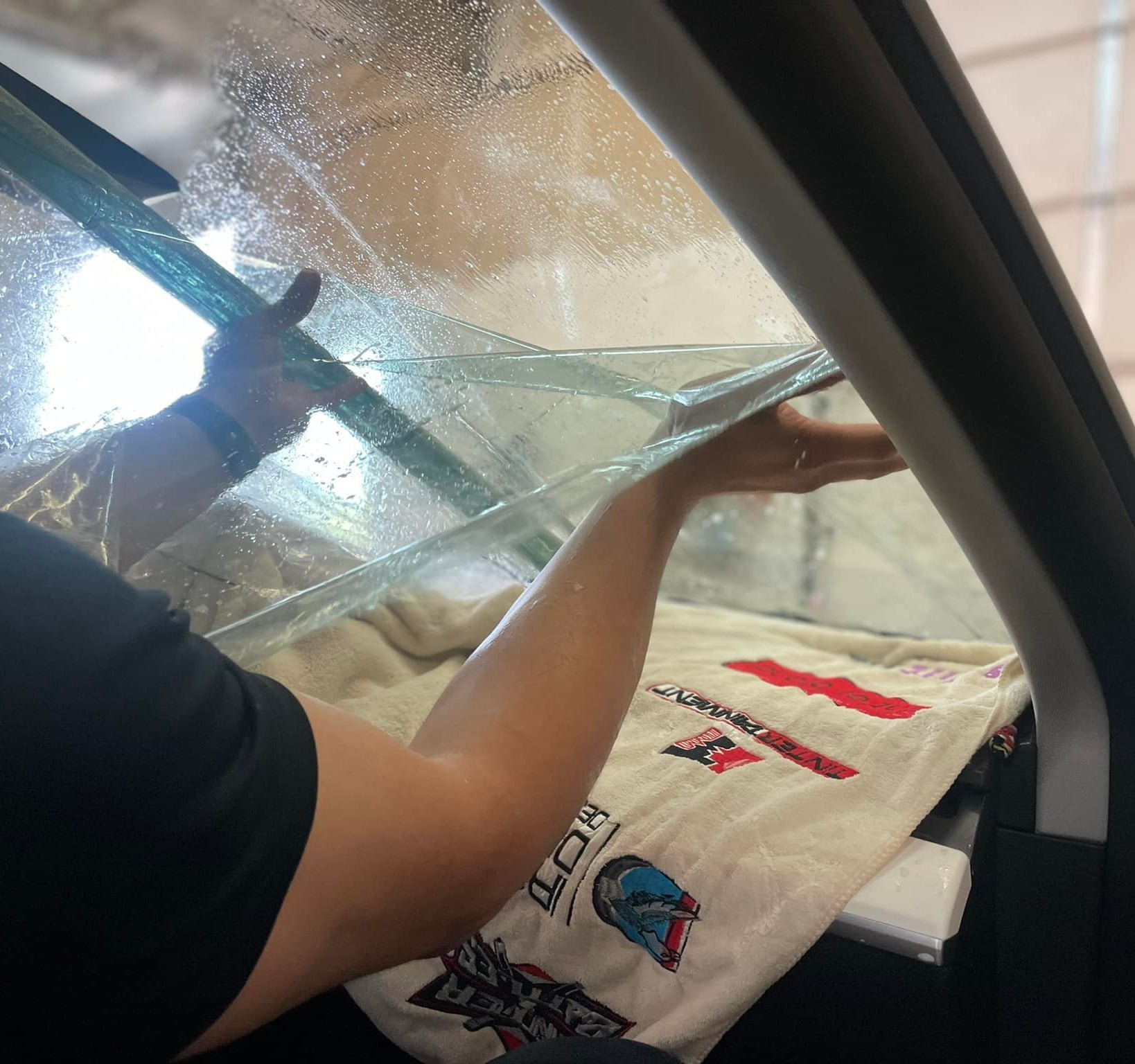 Hands applying window tint to a car's windshield, showcasing the meticulous installation process at Luxe Auto Salon, emphasizing quality craftsmanship and attention to detail in auto care services.